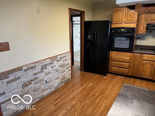 kitchen featuring decorative backsplash, light hardwood / wood-style floors, extractor fan, and black appliances