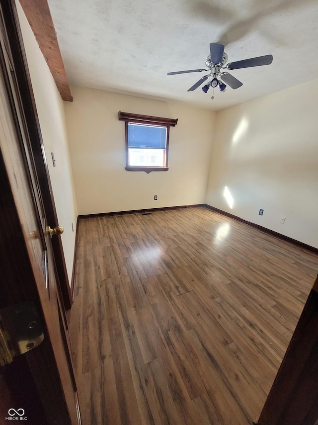 empty room featuring ceiling fan, dark hardwood / wood-style flooring, and beamed ceiling