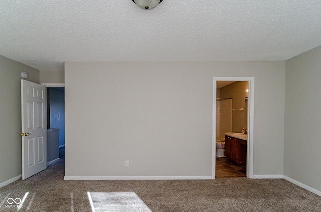 unfurnished bedroom with ensuite bathroom, dark carpet, and a textured ceiling