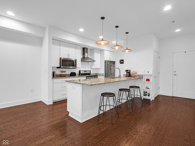 kitchen featuring dark wood-type flooring, white cabinets, wall chimney range hood, hanging light fixtures, and appliances with stainless steel finishes