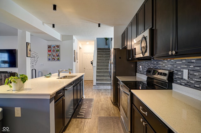 kitchen featuring sink, stainless steel appliances, tasteful backsplash, light stone counters, and light hardwood / wood-style floors