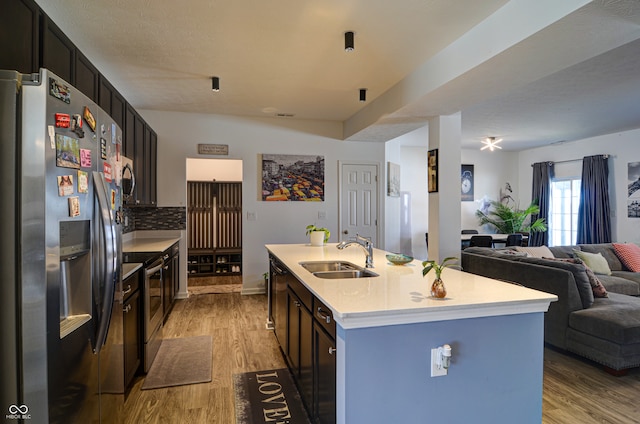 kitchen with sink, stainless steel appliances, light hardwood / wood-style floors, decorative backsplash, and a center island with sink