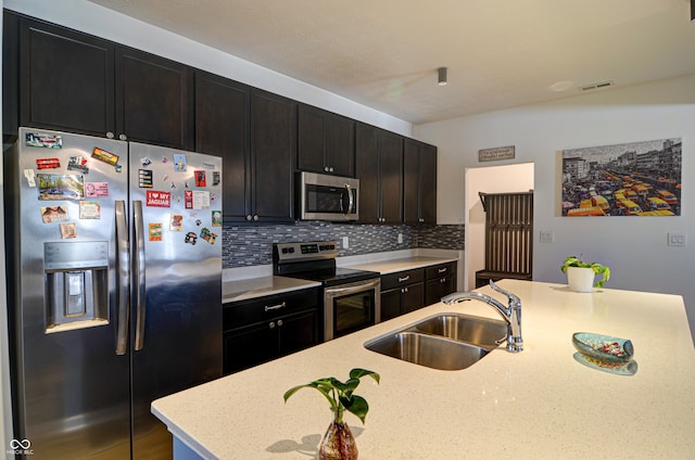 kitchen featuring light stone countertops, sink, stainless steel appliances, decorative backsplash, and a center island with sink