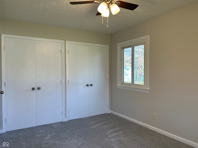 unfurnished bedroom featuring dark colored carpet, two closets, and ceiling fan