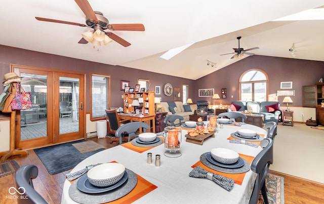 dining area with ceiling fan, lofted ceiling with skylight, and light hardwood / wood-style flooring