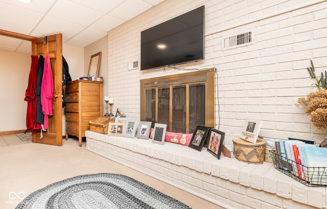 interior space featuring a brick fireplace, carpet floors, and a drop ceiling