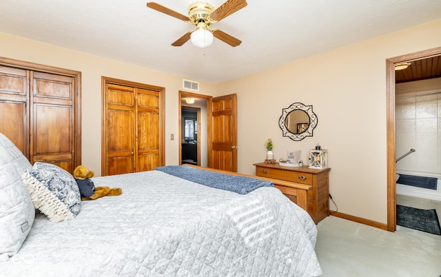 bedroom featuring ensuite bathroom, two closets, ceiling fan, and light colored carpet