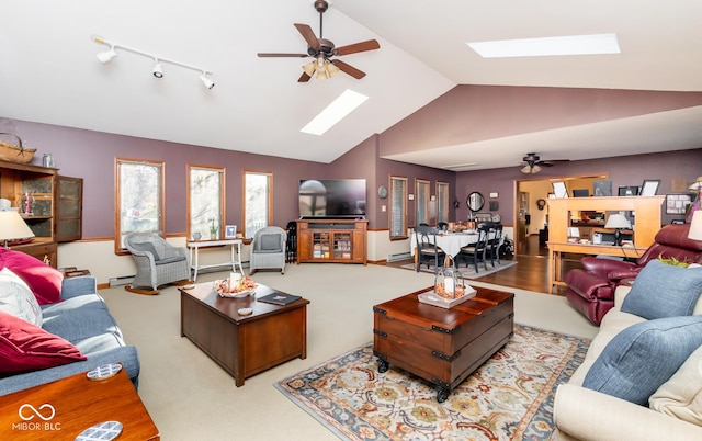 living room featuring lofted ceiling with skylight, rail lighting, baseboard heating, and ceiling fan