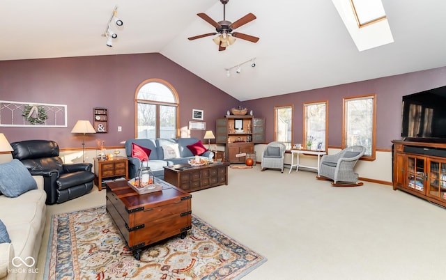 carpeted living room with rail lighting, vaulted ceiling with skylight, ceiling fan, and a wealth of natural light