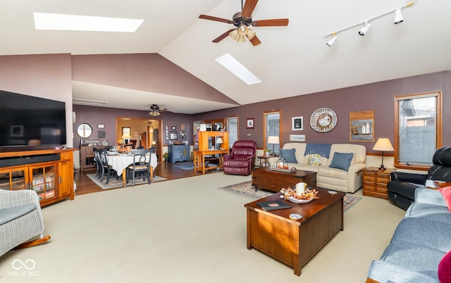 carpeted living room with ceiling fan, lofted ceiling with skylight, and track lighting