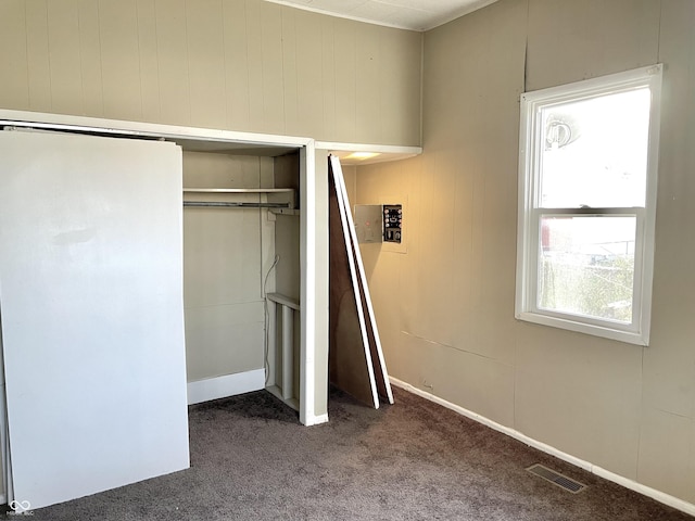 unfurnished bedroom with wood walls, carpet flooring, and a closet