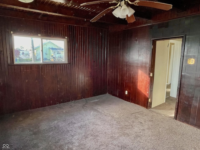 carpeted empty room featuring wooden walls and ceiling fan