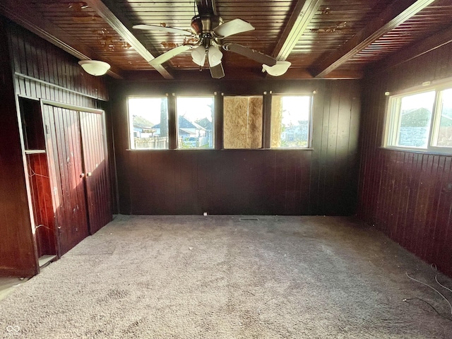 spare room with ceiling fan, beamed ceiling, carpet flooring, and wooden walls