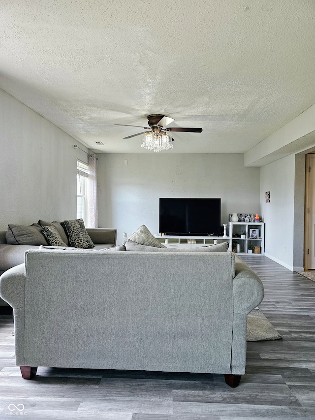 living room with a textured ceiling, ceiling fan, and dark wood-type flooring