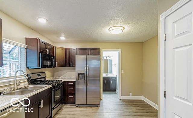 kitchen featuring light wood-type flooring, a textured ceiling, stainless steel appliances, dark brown cabinetry, and sink