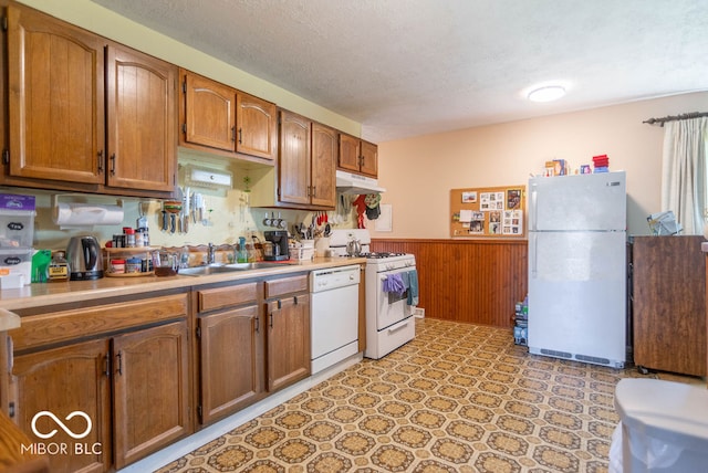 kitchen featuring a textured ceiling, white appliances, wood walls, and sink