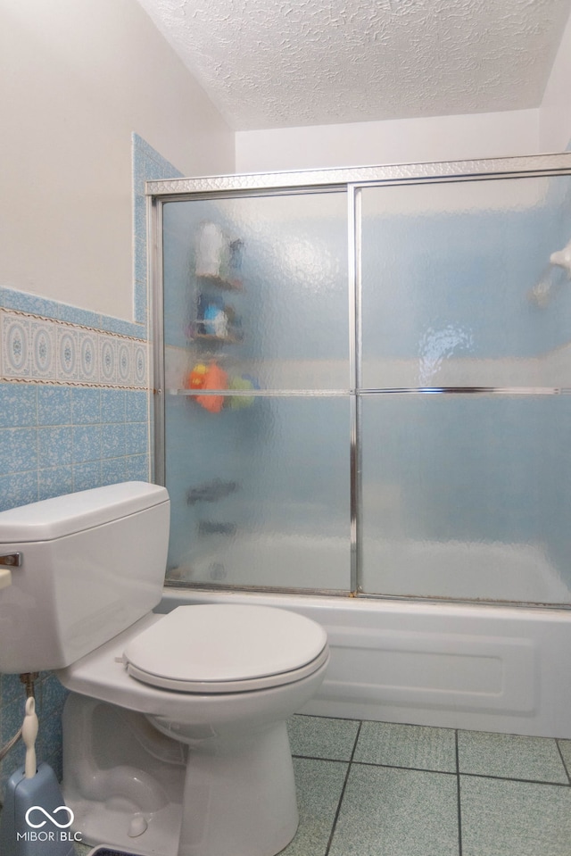 bathroom with tile patterned floors, a textured ceiling, tile walls, enclosed tub / shower combo, and toilet