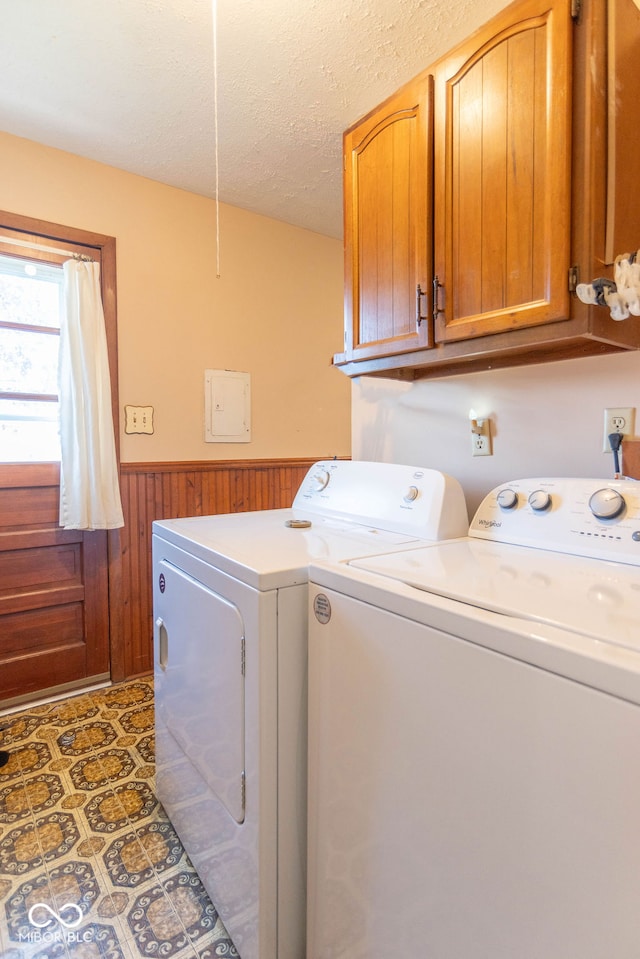 laundry area with wooden walls, cabinets, a textured ceiling, and independent washer and dryer