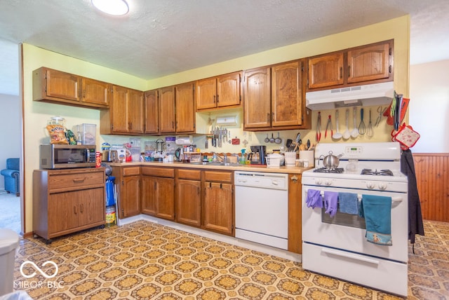 kitchen featuring a textured ceiling, white appliances, wooden walls, and sink