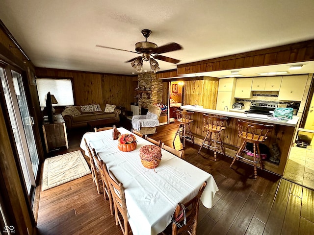 dining area featuring dark hardwood / wood-style floors, ceiling fan, and wooden walls