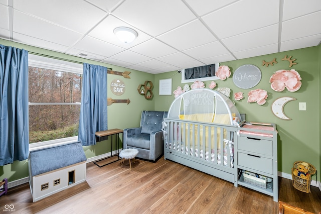 bedroom with a crib, wood-type flooring, and a paneled ceiling