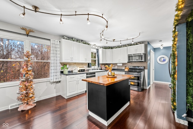 kitchen with wooden counters, appliances with stainless steel finishes, white cabinetry, and a healthy amount of sunlight