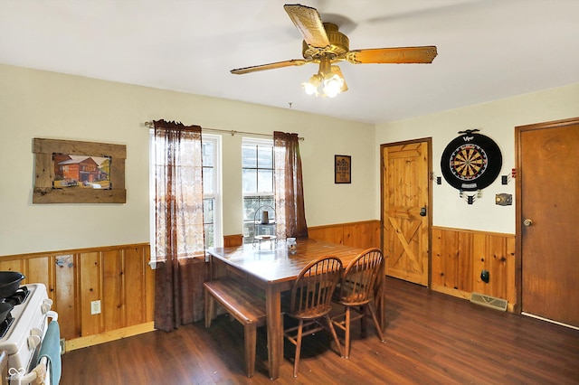 dining space featuring ceiling fan, dark wood-type flooring, and wood walls