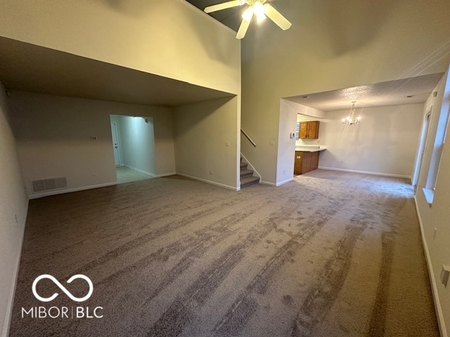 unfurnished living room featuring ceiling fan with notable chandelier, carpet, and a high ceiling