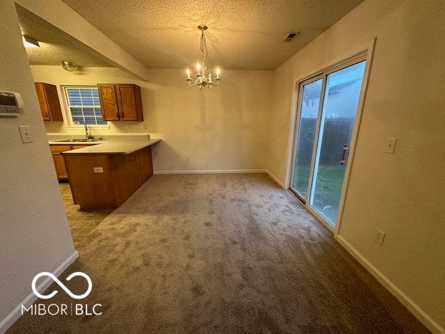 kitchen with a notable chandelier, decorative light fixtures, light colored carpet, and kitchen peninsula