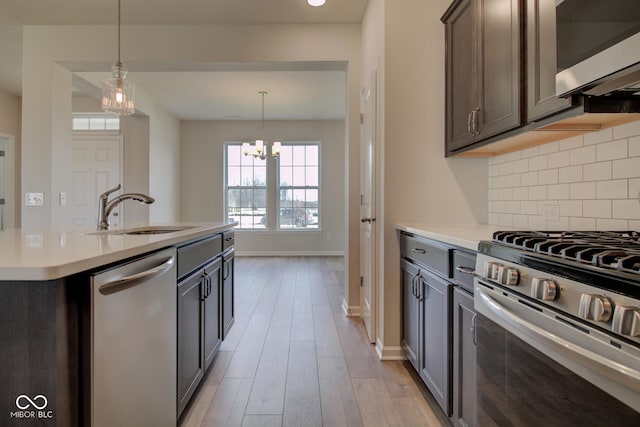 kitchen featuring a center island with sink, sink, light hardwood / wood-style flooring, appliances with stainless steel finishes, and a chandelier