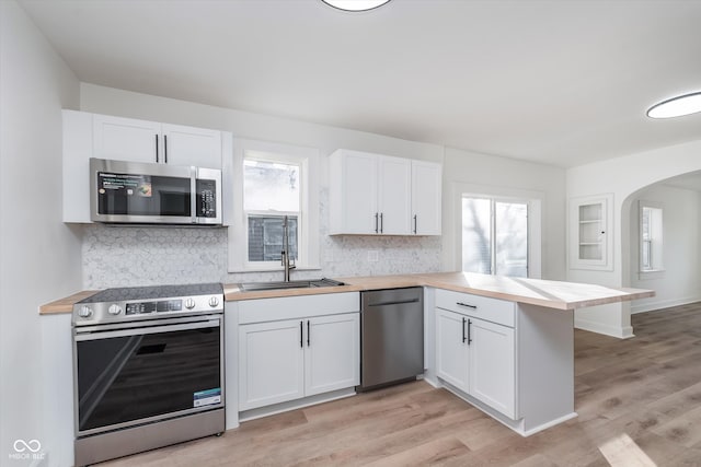 kitchen with kitchen peninsula, appliances with stainless steel finishes, light wood-type flooring, and white cabinets