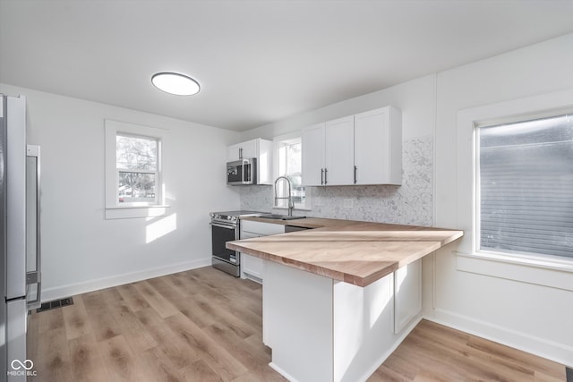 kitchen featuring butcher block counters, sink, light hardwood / wood-style flooring, white cabinets, and appliances with stainless steel finishes