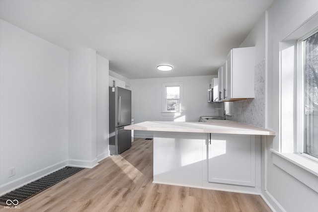 kitchen with a breakfast bar, white cabinetry, light hardwood / wood-style flooring, high end fridge, and kitchen peninsula