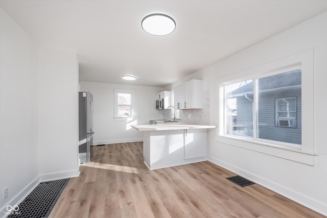 kitchen with white cabinetry, tasteful backsplash, kitchen peninsula, light hardwood / wood-style floors, and a breakfast bar area