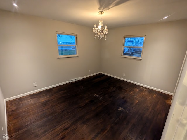 empty room with dark wood-type flooring and a notable chandelier