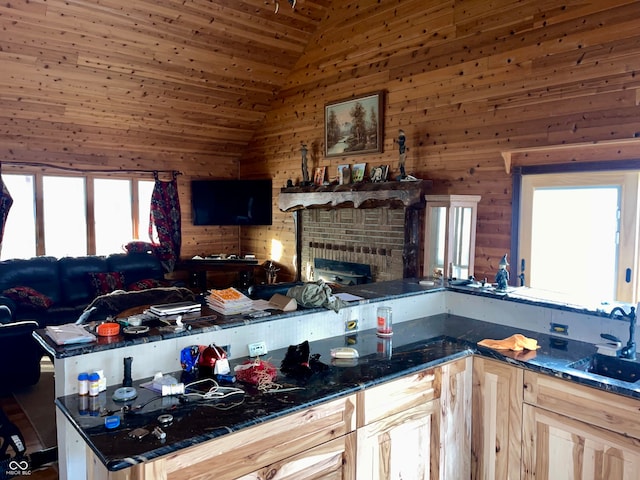 kitchen with wooden walls, sink, light brown cabinets, dark stone countertops, and lofted ceiling