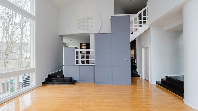 unfurnished bedroom with light wood-type flooring, a towering ceiling, and multiple windows