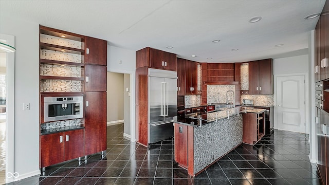 kitchen featuring dark tile patterned floors, an island with sink, decorative backsplash, custom range hood, and appliances with stainless steel finishes