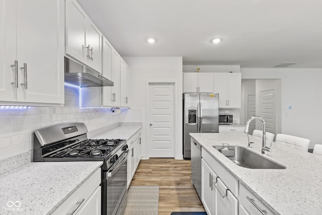 kitchen with sink, light hardwood / wood-style flooring, appliances with stainless steel finishes, light stone counters, and white cabinetry