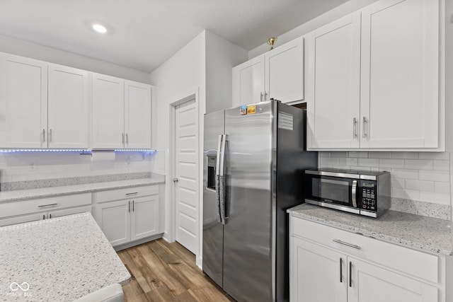 kitchen with light hardwood / wood-style flooring, decorative backsplash, light stone countertops, white cabinetry, and stainless steel appliances