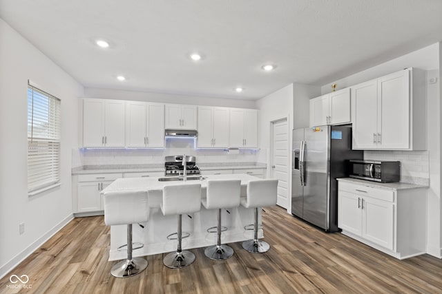 kitchen with a center island with sink, hardwood / wood-style flooring, white cabinetry, and appliances with stainless steel finishes