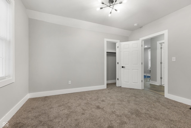 unfurnished bedroom featuring a spacious closet, a notable chandelier, lofted ceiling, a closet, and carpet