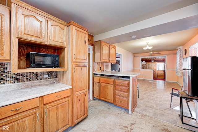 kitchen featuring ceiling fan, kitchen peninsula, backsplash, and stainless steel refrigerator