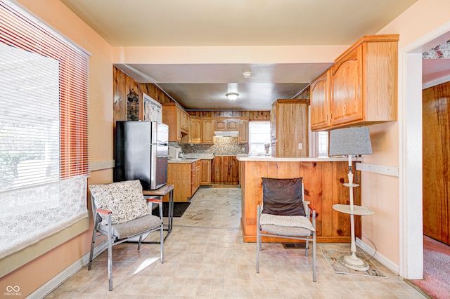 kitchen with decorative backsplash, stainless steel fridge, kitchen peninsula, and a healthy amount of sunlight