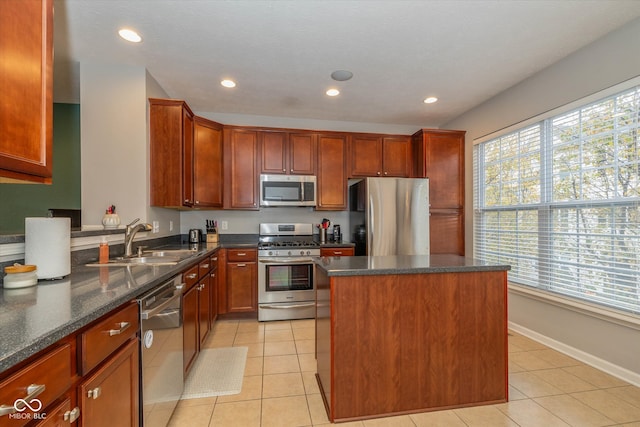 kitchen with sink, a center island, dark stone countertops, light tile patterned floors, and appliances with stainless steel finishes