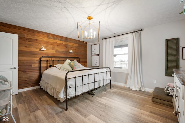 bedroom with a textured ceiling, light wood-type flooring, a chandelier, and wooden walls