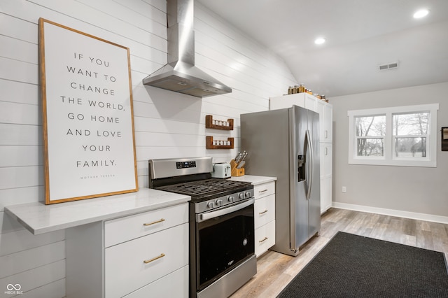 kitchen with wall chimney range hood, white cabinetry, appliances with stainless steel finishes, and vaulted ceiling