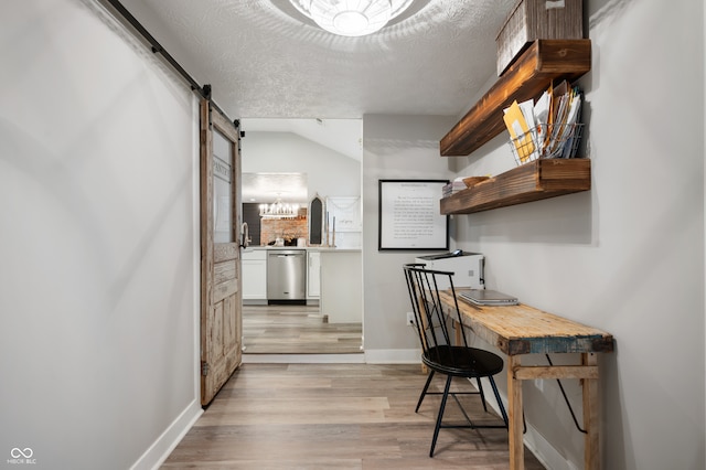 interior space featuring a textured ceiling, light hardwood / wood-style flooring, lofted ceiling, and a barn door