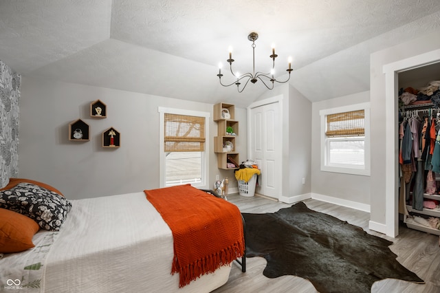 bedroom with vaulted ceiling, light hardwood / wood-style floors, an inviting chandelier, a textured ceiling, and a closet