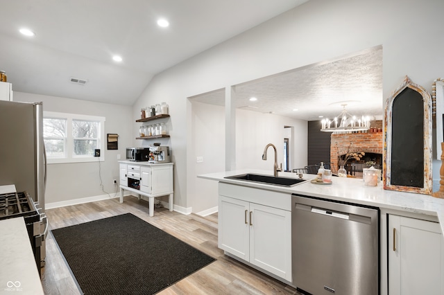 kitchen featuring white cabinetry, appliances with stainless steel finishes, decorative light fixtures, lofted ceiling, and sink